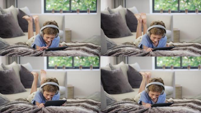 小男孩在床上带着耳机使用数字平板电脑