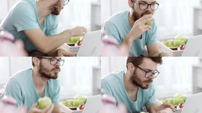使用笔记本电脑吃苹果的男人