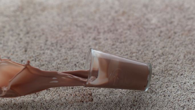 一杯巧克力牛奶以慢动作洒在地毯上