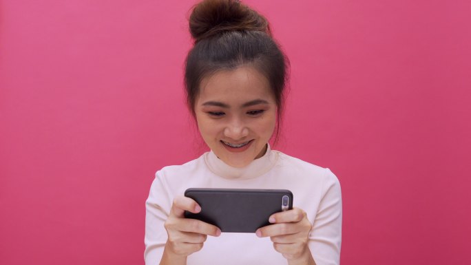 女人在粉色背景上玩智能手机游戏