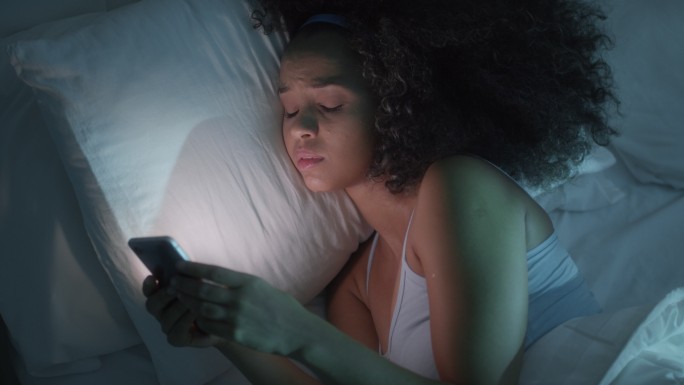 年轻的妇女在床上用智能手机发短信