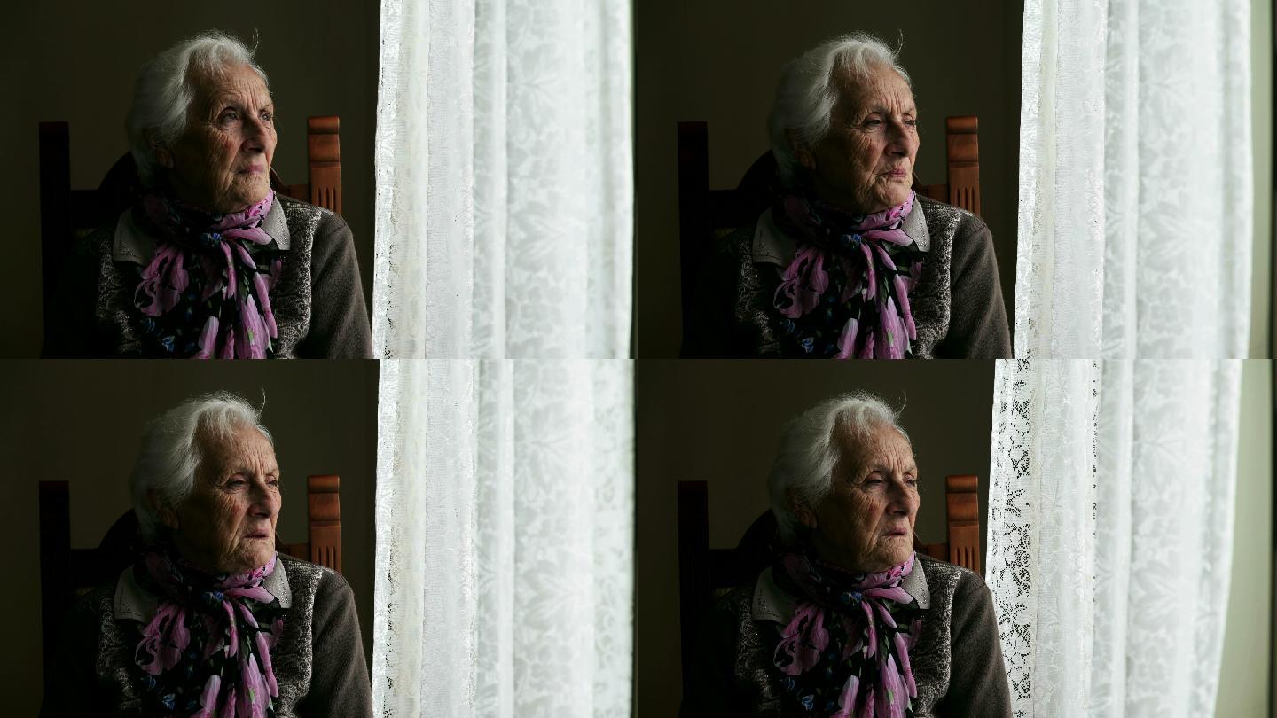坐在窗边的悲伤而沉思的老+妇人