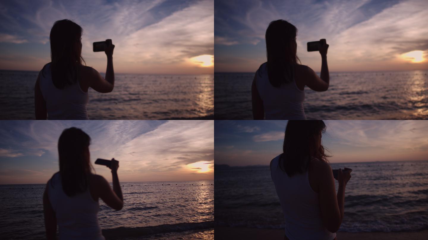 在海滩拍日落照片的年轻女子