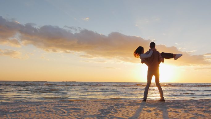 在日落的沙滩上男子拥抱女朋友旋转