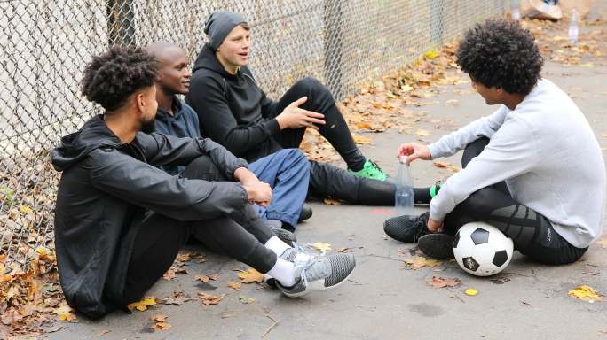 足球运动员靠着栅栏坐着聊天