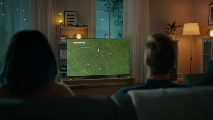晚上，夫妇坐在沙发上看电视上的足球比赛