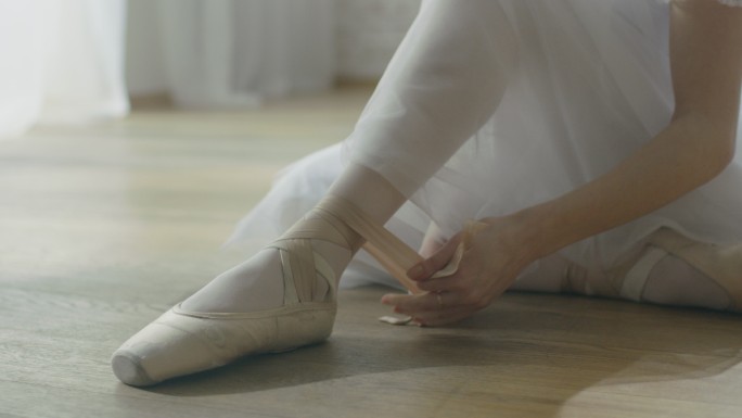 芭蕾舞演员坐在木地板上系鞋带