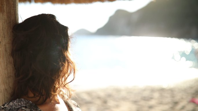 日落时女子坐在沙滩上的遮阳伞下