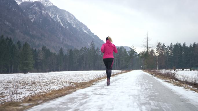 一名女跑步者在雪地上的人行道上跑步。