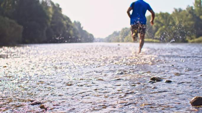 男子慢跑过河跑步鞋飞溅在浅水的河流速度湿