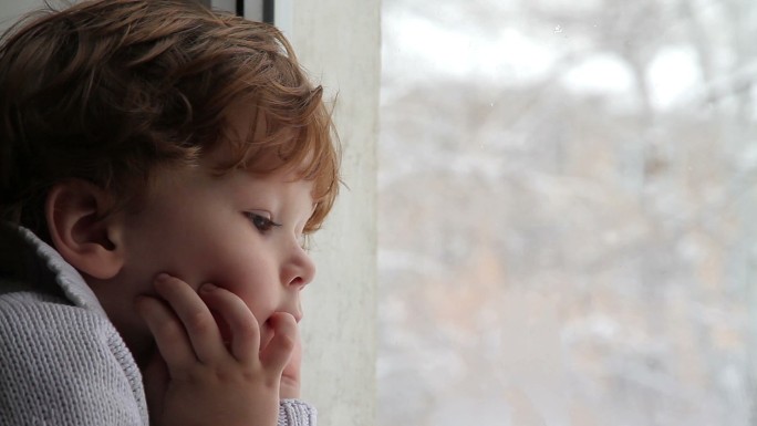 男孩看着窗外飘落的雪