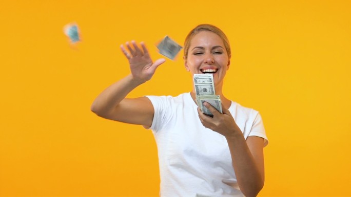 在橙色背景下扔美元的快乐女人