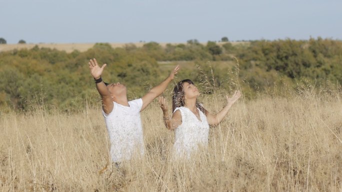 一男一女穿着白衣服，站在草地上伸开双臂