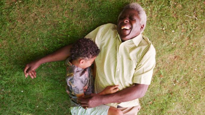 男孩和爷爷躺在草地上微笑着，头顶特写