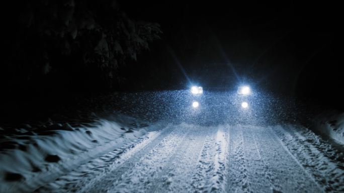 雪天晚上在雪路上行驶的汽车