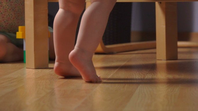 赤脚蹒跚学步的孩子踮着脚尖靠近扶手椅