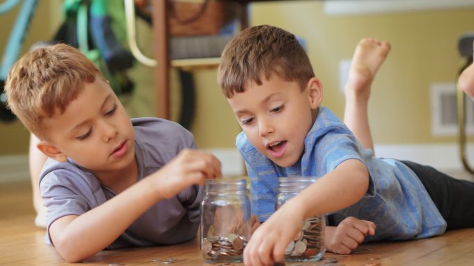 两个小男孩子把硬币装进罐子里