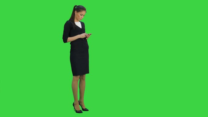 女人一边看手机，一边走在绿色屏幕上