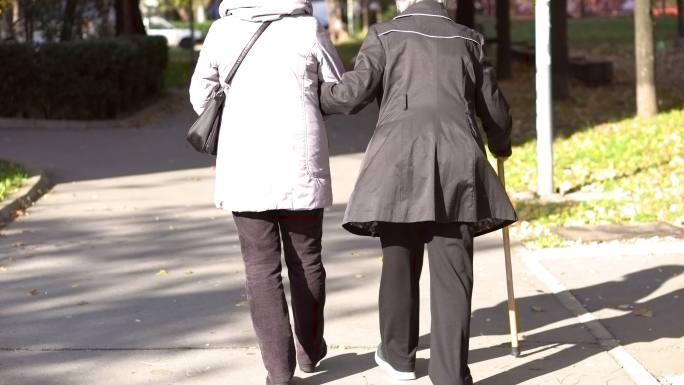 老年妇女与女理疗师在户外散步的后视图。