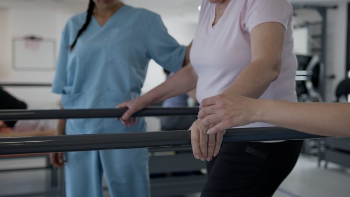 女性患者在双杠和治疗师的帮助下缓慢行走