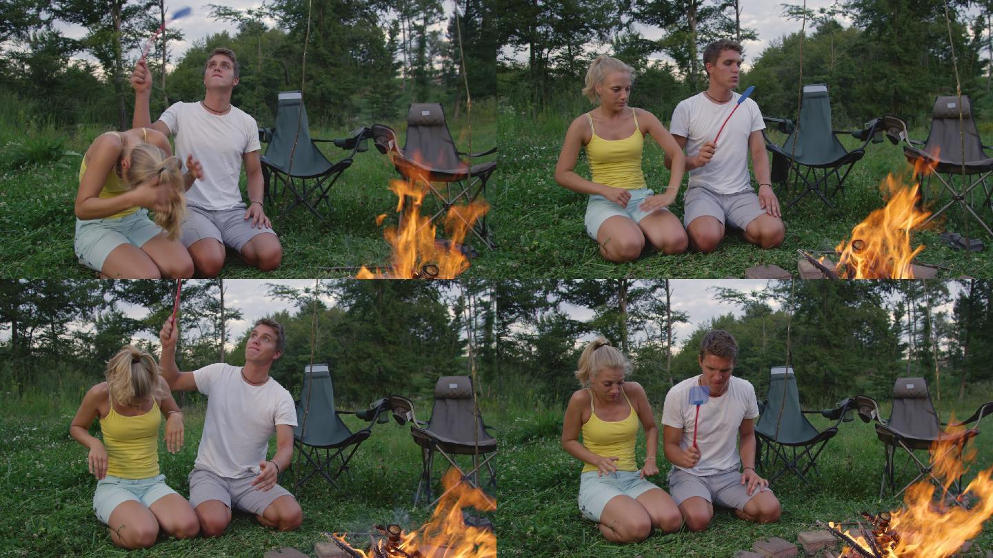 一男一女坐在营火旁挥舞苍蝇拍驱赶虫子