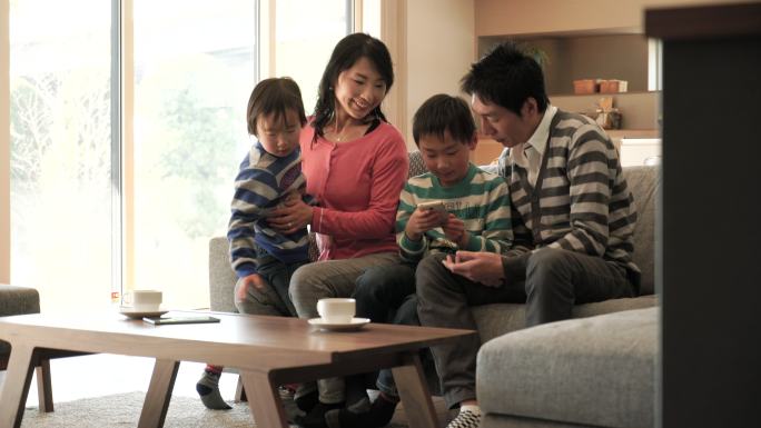 一家人在家的沙发上一起玩平板电脑