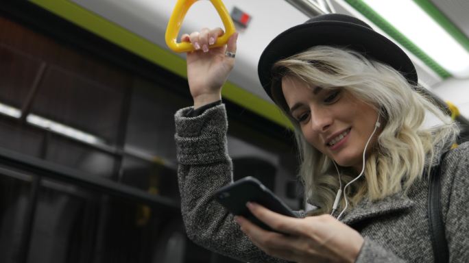 在地铁里戴着耳机听音乐和浏览手机的女孩