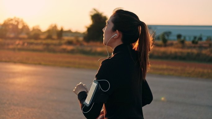 戴着耳机在日落时分奔跑的女人