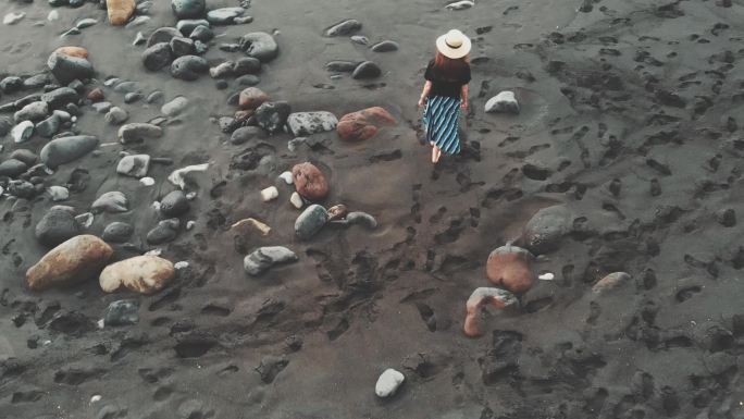 带着帽子的女孩，走在火山沙的黑色海滩。