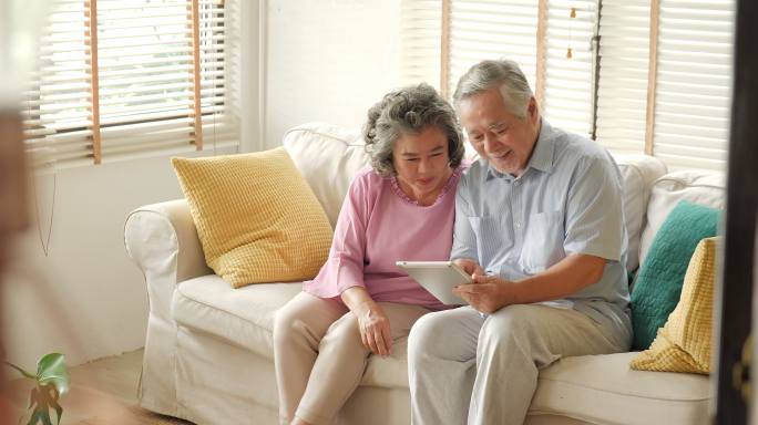 老年夫妇坐在沙发上用平板电脑聊天微笑