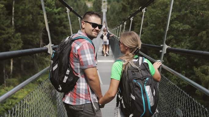一男一女背着背包沿着一座金属吊桥行走