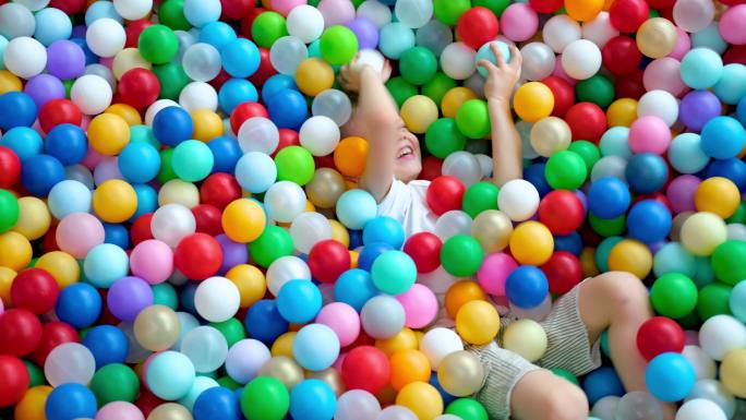 小男孩躺在彩色球池里玩耍
