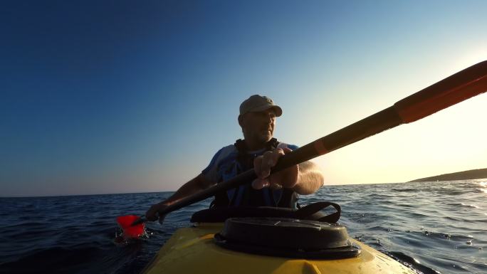 傍晚的阳光下，一个老人在海上划独木舟