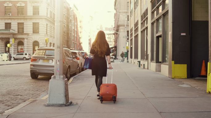 一个女人拖着带轮子的手提箱穿过阳光明媚的
