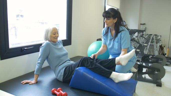 护士协助老年妇女进行腿部锻炼