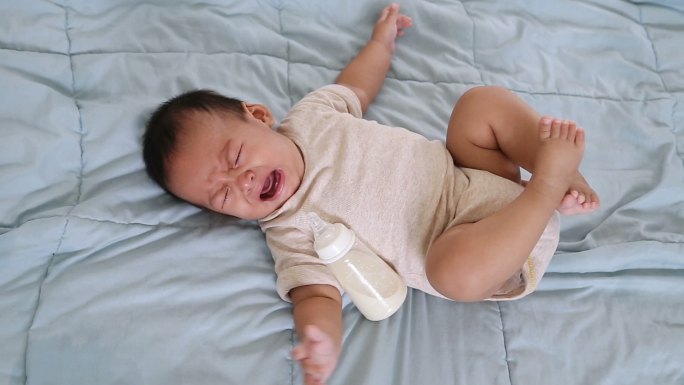 男婴抱着奶瓶在床上哭