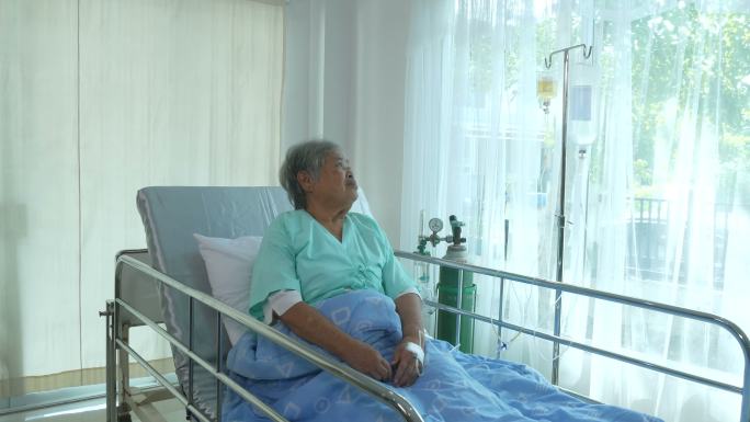 老年女病人坐在病床上担忧地看着窗外