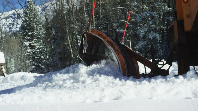 一辆拖拉机在山上的森林旁铲雪
