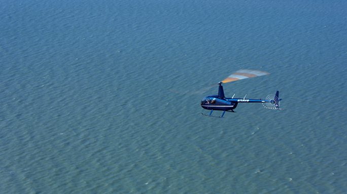 空中直升机在阳光下飞越海面