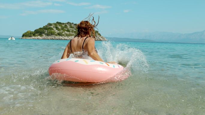 阳光明媚的夏日海洋中，女人跳上充气游泳圈