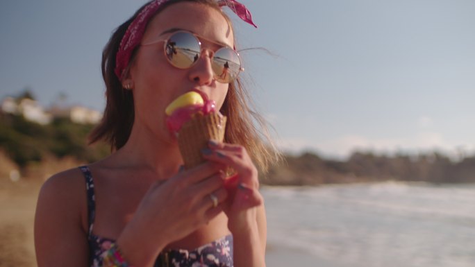 年轻的时髦女人吃冰淇淋在海滩散步
