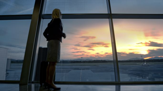 在机场透过玻璃墙观察日落的女商人