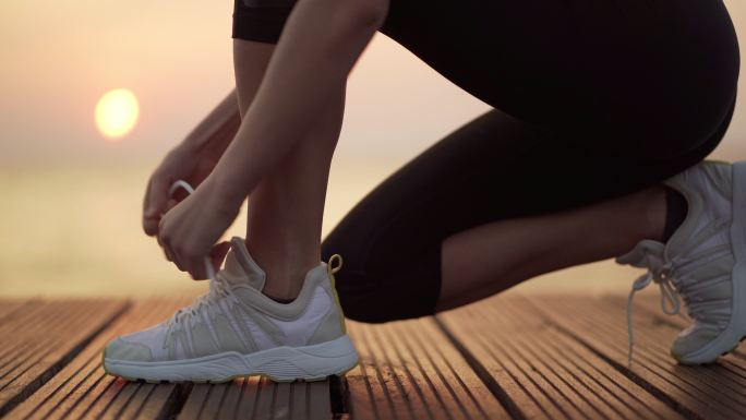 日落时分，年轻女子正在海边系鞋带慢跑。