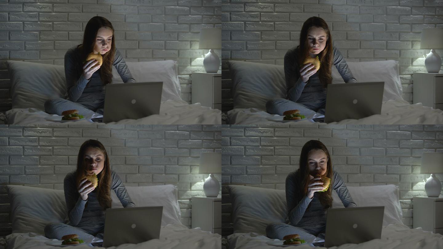 年轻女性晚上在床上上网时吃汉堡包