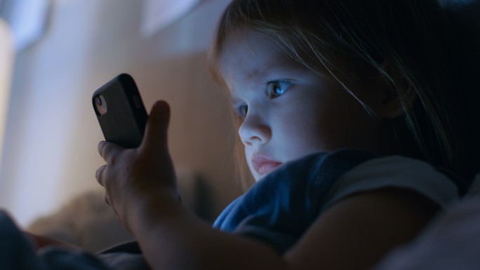 可爱的小女孩用智能手机看动画片