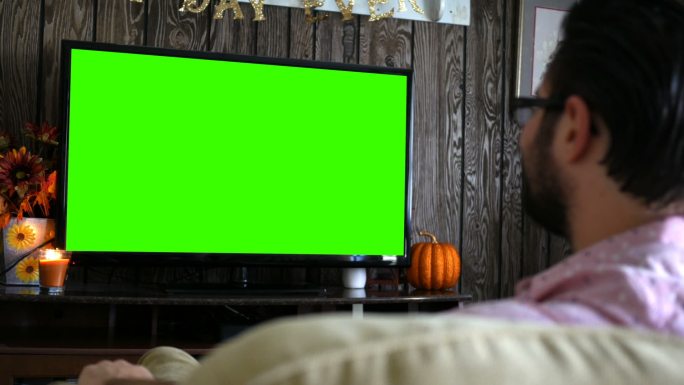男子正在看绿屏电视，拿着遥控器切换频道