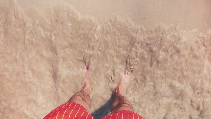 一个男人站在沙滩上，脚浸在水里的镜头。