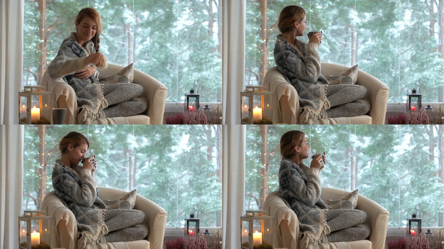 年轻的女人喝着咖啡穿着毛衣坐在大窗前