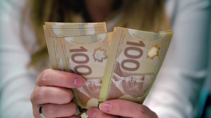 一个女人数着100张加拿大钞票的画面