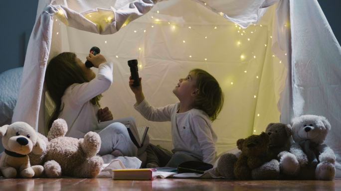 夜间两个小女孩在帐篷里玩手电筒